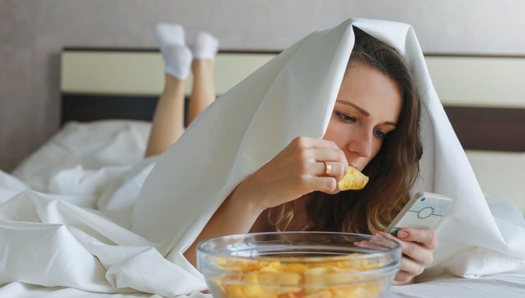 Frau isst Chips im Bett